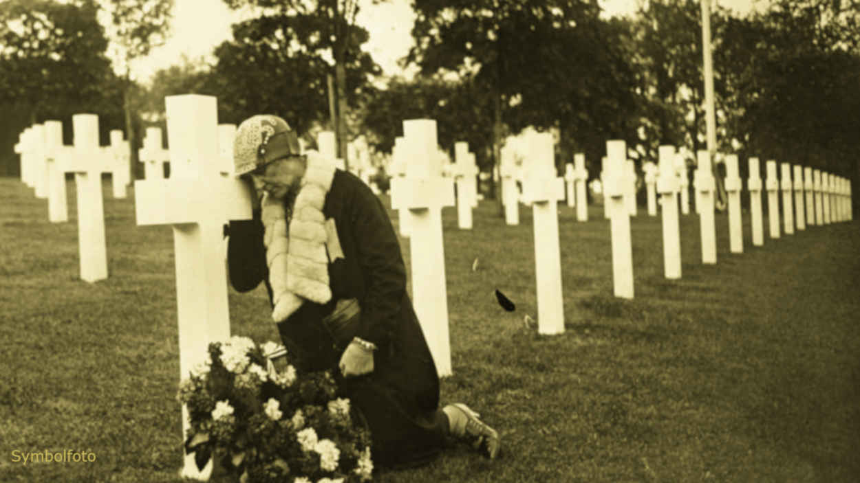 Ein Friedhof mit vielen Gräbern, auf dem eine Frau an einem Kreuz trauert.