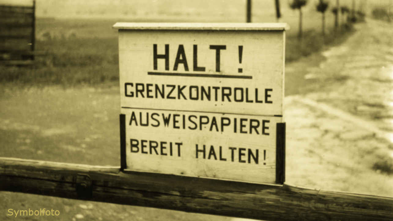 Schlagbaum an der Grenze mit einem Schild, auf dem steht: Halt! Grenzkontrolle, Ausweispapiere bereit halten!